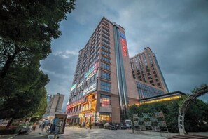 Un hôtel à plusieurs étages, doté d’une enseigne verticale bien visible, d’un restaurant situé au rez-de-chaussée et d’un espace de stationnement.