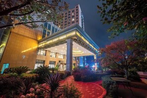 A modern hotel with a covered entrance, a red pathway, and surrounding greenery. - Puhua Hotel (Anshun)