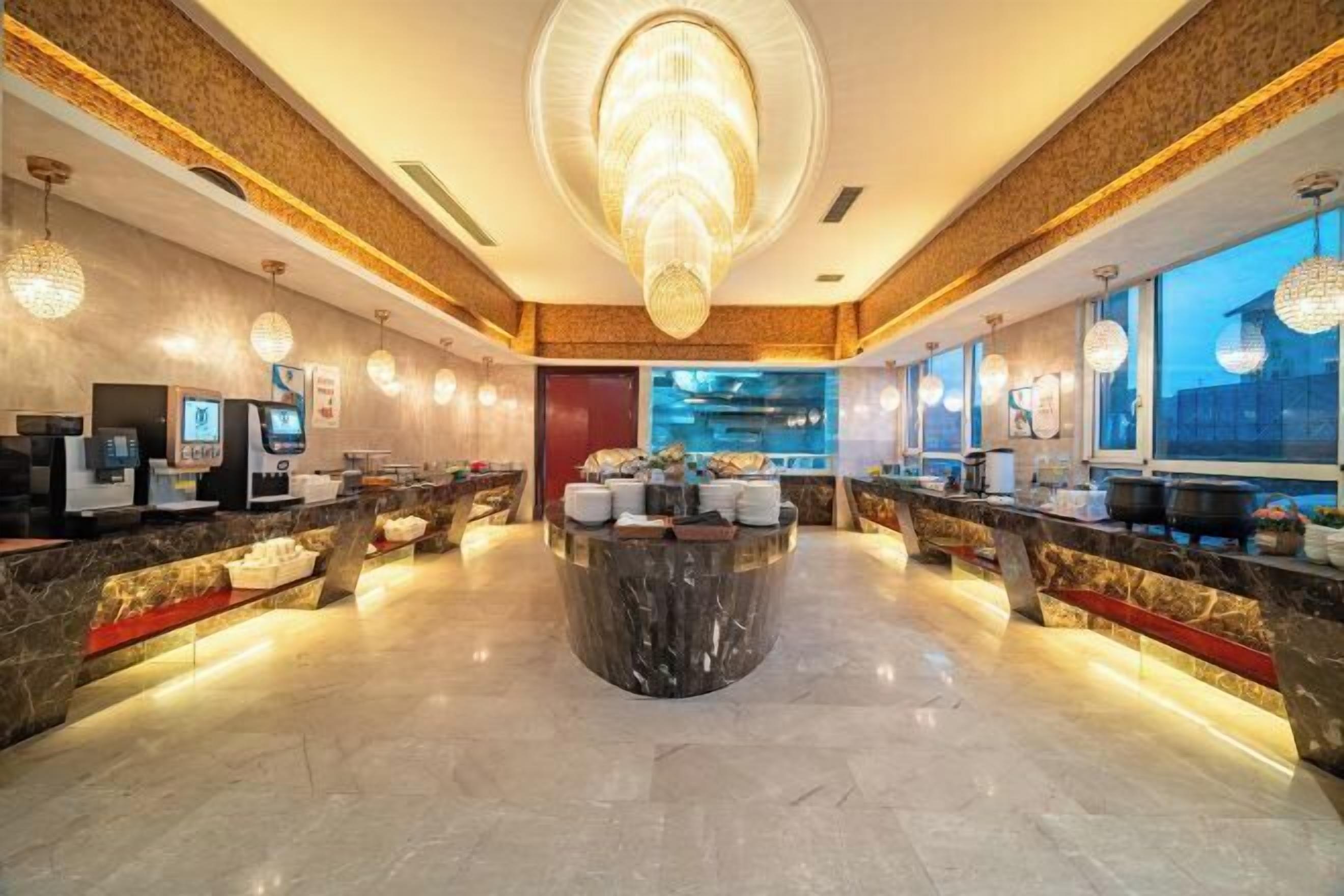 Eine Hotelhalle mit einem zentralen Marmor-Rezeptionstresen, moderner Beleuchtung und einem großen Kronleuchter.