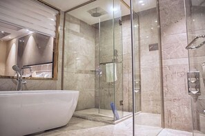 A modern bathroom with a freestanding bathtub, a glass-enclosed shower, and marble walls. - Puhua Hotel (Anshun)