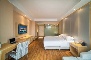 A hotel room with a bed, a desk with a laptop, a chair, a TV mounted on the wall, and a bedside table with a phone. - Puhua Hotel (Anshun)