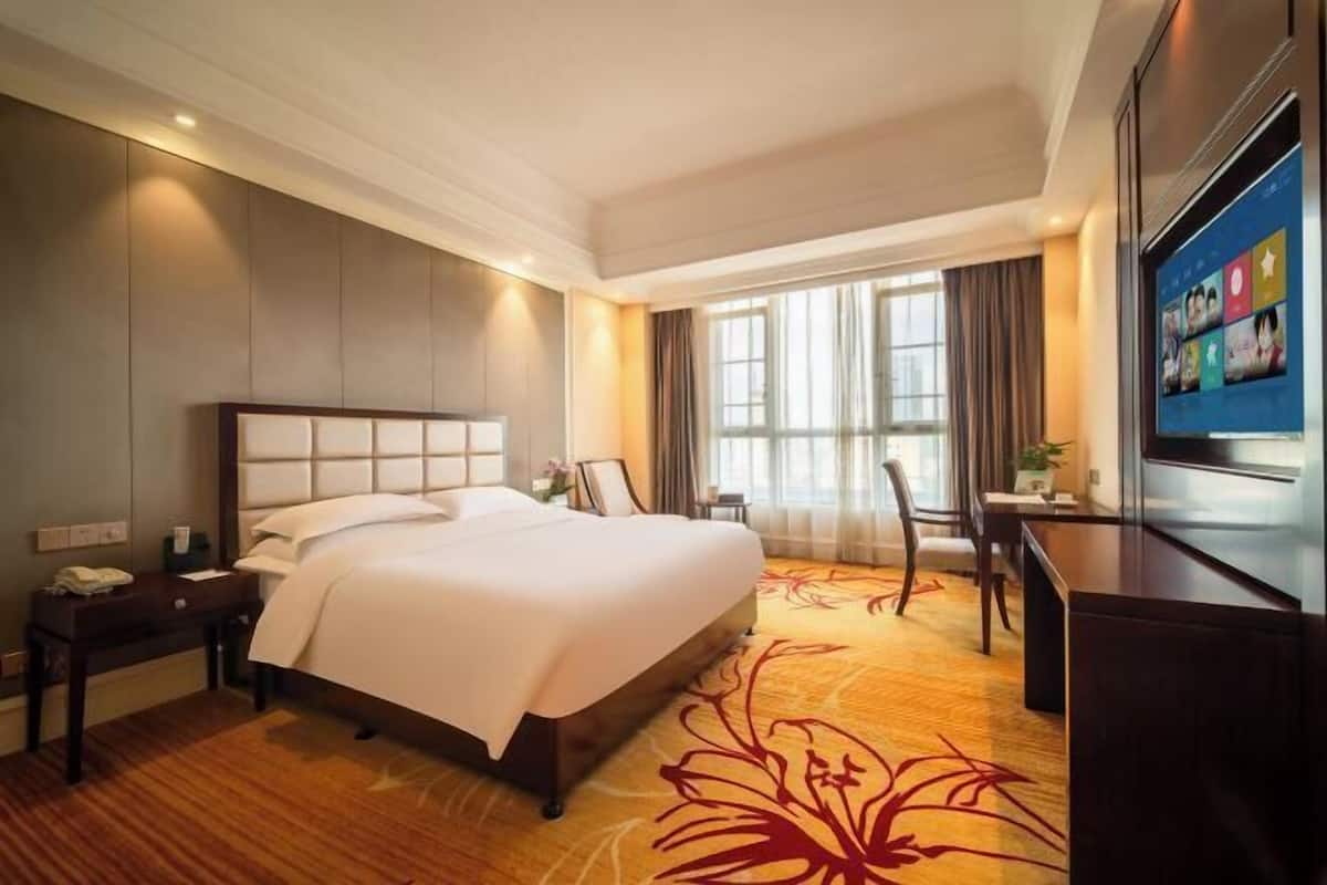 A hotel room with a large bed, a desk, a television, and a window with curtains.