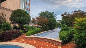 A courtyard with a swimming pool, surrounded by greenery and a tall building. - Puhua Hotel (Anshun)