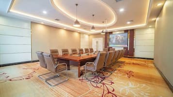 A conference room with a long table, chairs, a projector screen, and a carpet with a floral pattern.