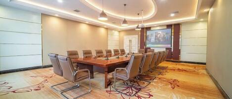 A conference room with a long table, chairs, a projector screen, and a carpet with a floral pattern.