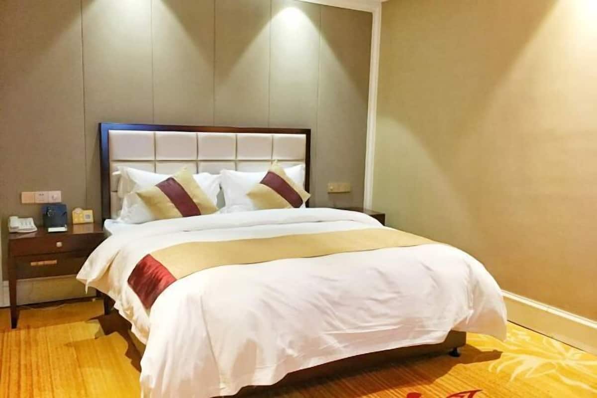 A hotel room with a bed, a nightstand, and a wall-mounted light.