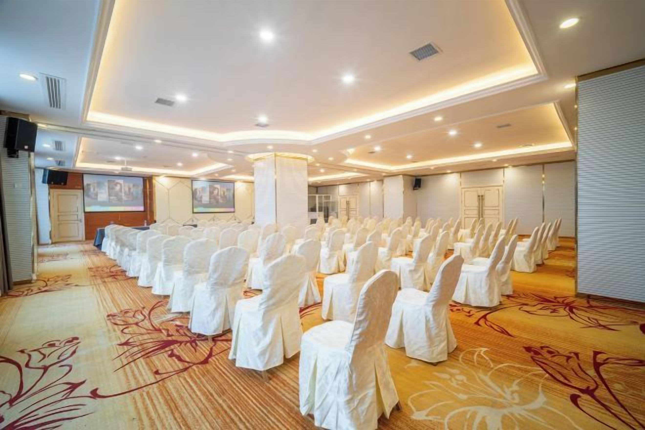 A conference room with rows of chairs, a carpeted floor, and a large screen.