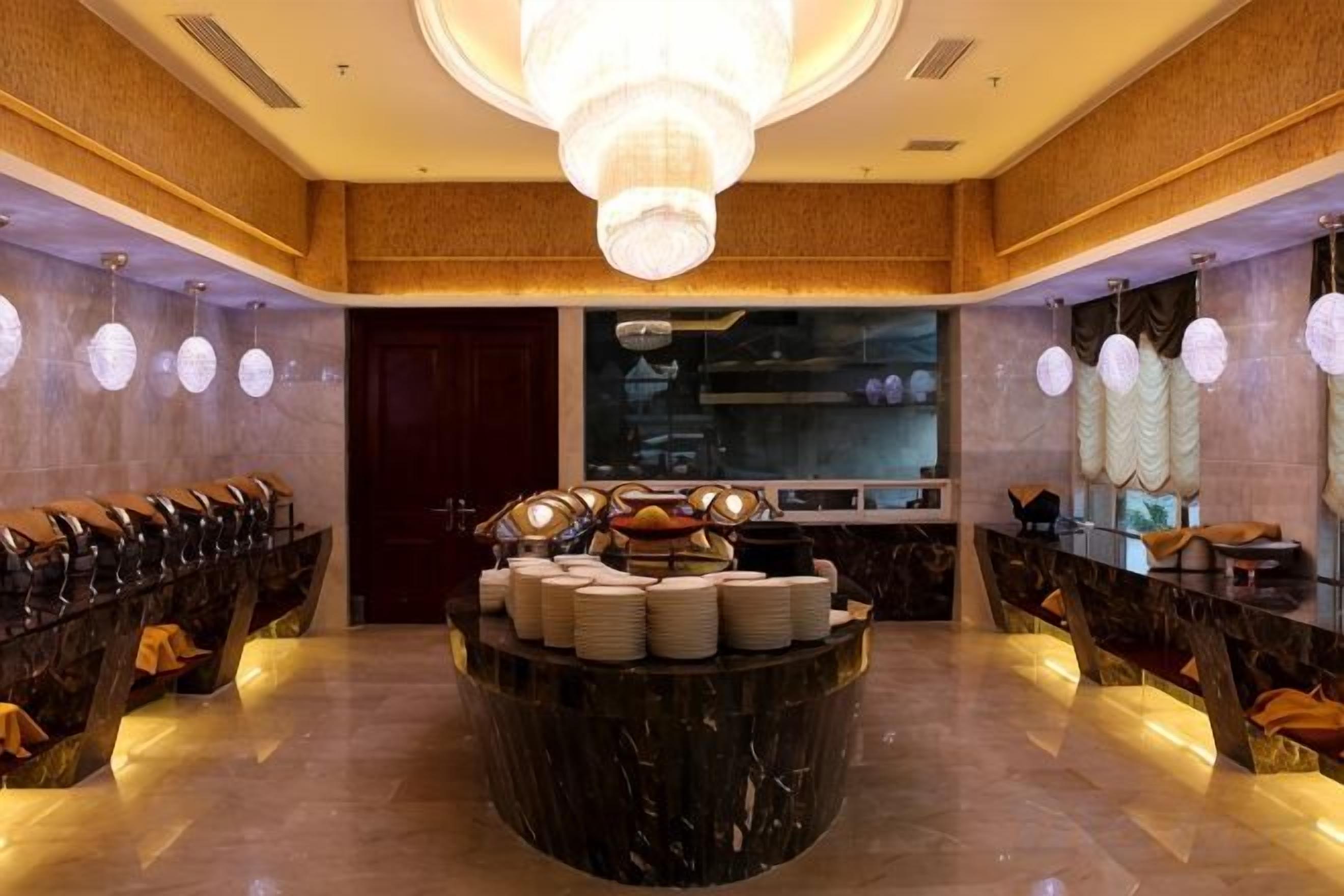 Un vestíbulo de hotel con un mostrador de recepción de mármol, una araña y una zona de buffet con platos y cuencos.
