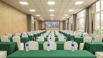A conference room with rows of tables, chairs, and water bottles, equipped with a large screen at the front.