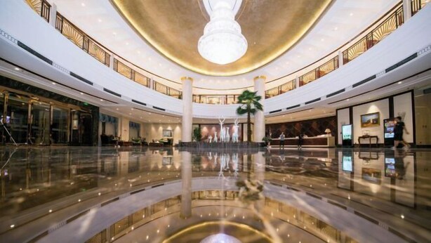 A spacious, modern hotel lobby with a central fountain, multiple floors, and a high ceiling with a large chandelier. - Puhua Hotel (Anshun)