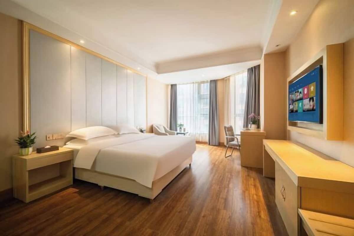 A modern hotel room with a large bed, bedside tables, a desk, and a TV.