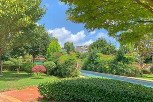 Un jardín ajardinado con un sendero, árboles y un edificio al fondo.