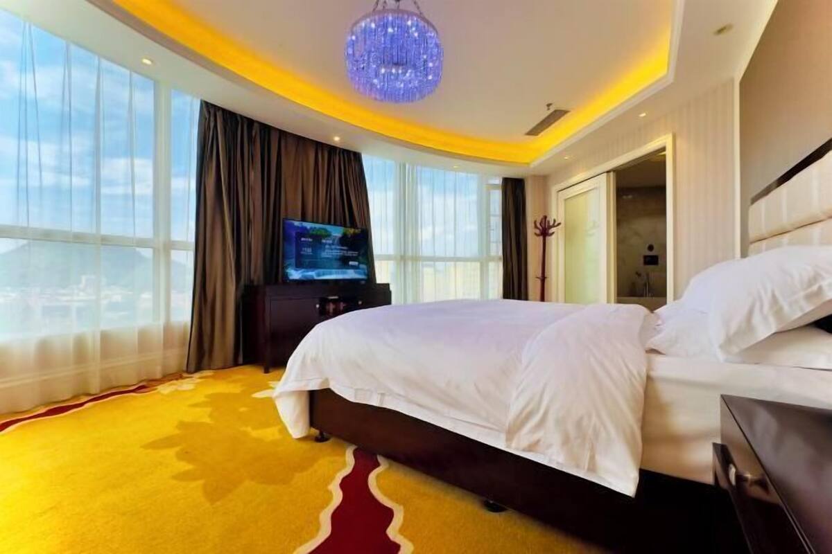 A modern hotel room with a large bed, a television, and a view of the city.