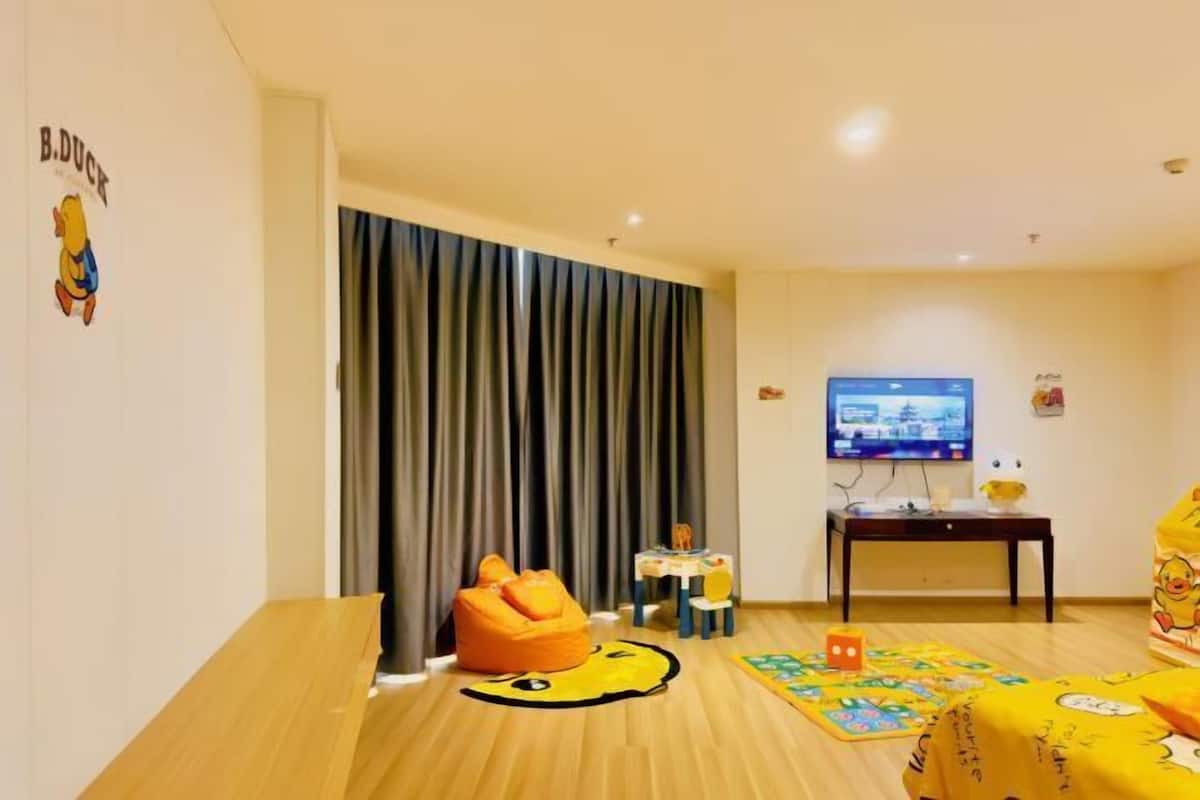 A room with a wooden floor, a television, a sofa, a small table, and a curtain.