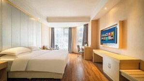 A hotel room with a large bed, a desk, a chair, a TV, and a window. - Puhua Hotel (Anshun)
