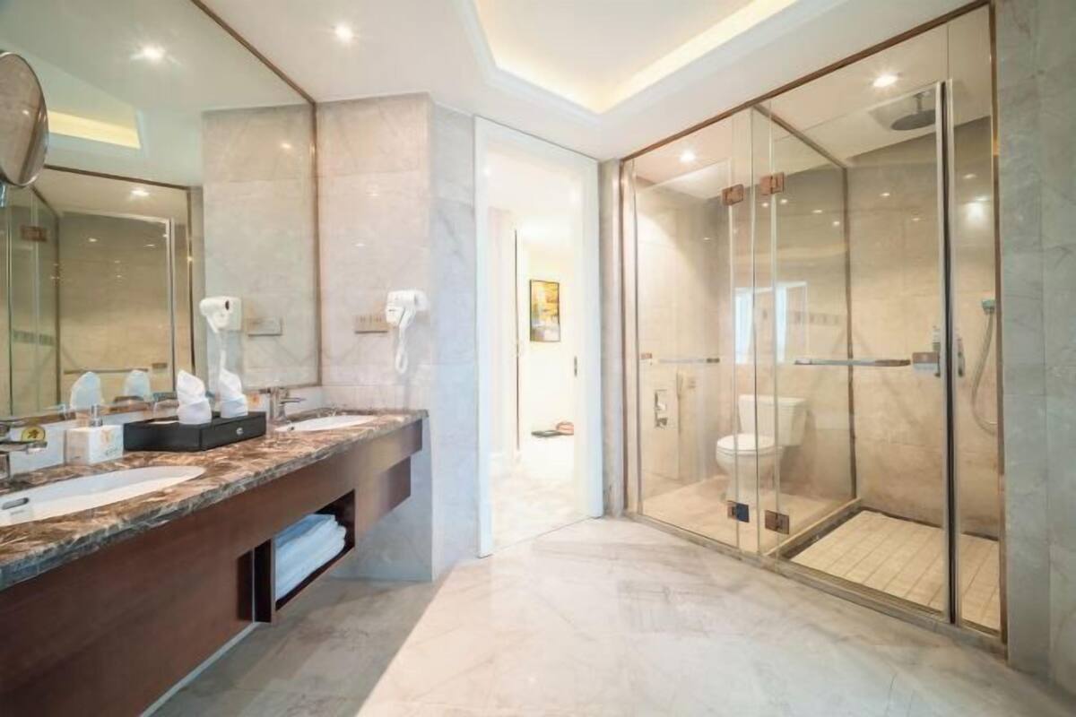 A modern bathroom with a marble countertop, a glass-enclosed shower, and a large mirror.