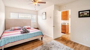 A bedroom with a bed, a ceiling fan, a window with blinds, a door leading to a kitchen, and a rug on the floor. - Stay in the Heart of Hillcrest! San Diego (San Diego)