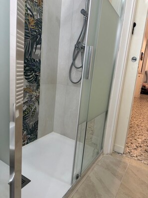 Una ducha con puerta de vidrio, cabezal de ducha y pared de azulejos.