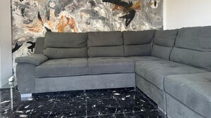 Un salon moderne avec un canapé d’angle gris, un grand tableau abstrait accroché au mur et un sol en marbre noir.