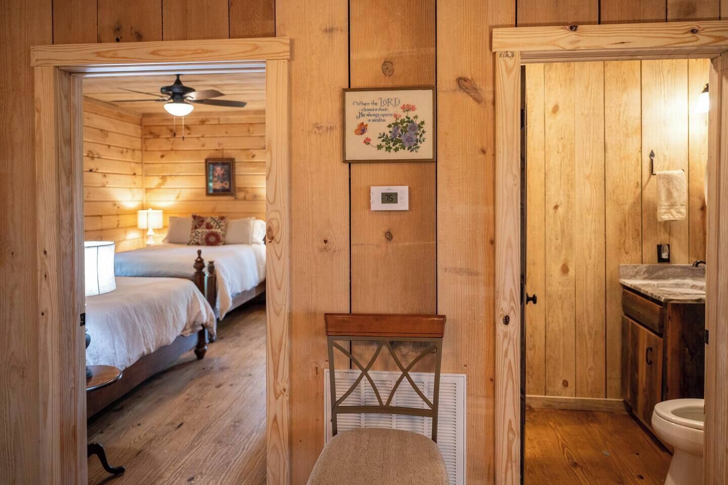 A wooden cabin with two bedrooms, a small bathroom, and a ceiling fan.