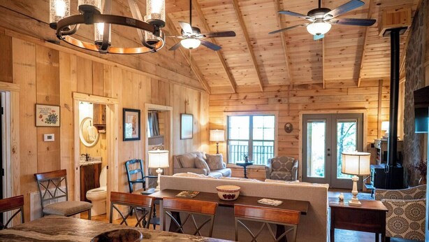 A cozy cabin interior with wooden walls, a dining area, a living room with a sofa, and a fireplace. - Pinhoti Ridge Retreat Cabin 2, Skyline (Talladega)