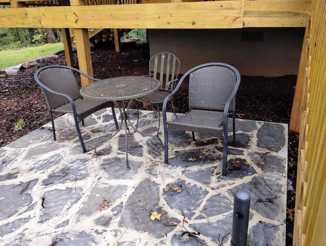A stone patio with metal chairs and a table, surrounded by a wooden deck.