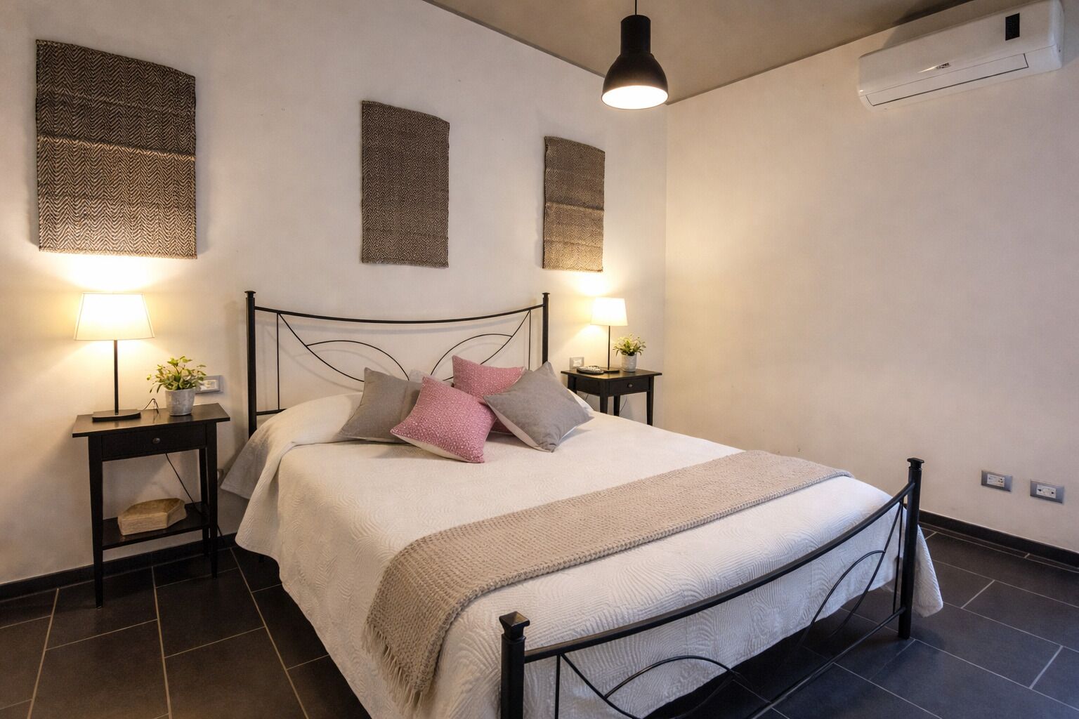 Una camera da letto ordinata con un letto, comodini, lampade e condizionatori fissati al muro.