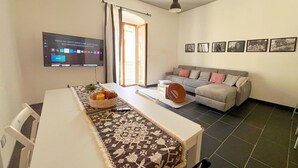 Un salon moderne avec un canapé, un téléviseur fixé au mur et une table à manger agrémentée d’un chemin de table à motifs.