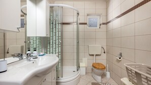 Et moderne badeværelse med en glasbrusekabine, et toilet med træsæde og en vask med spejl.