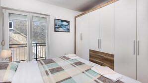 Une chambre à coucher avec un lit, une armoire en bois, un tableau et un balcon donnant sur des arbres.