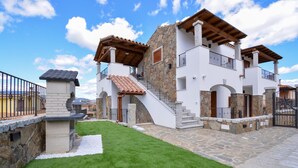 Une maison à deux étages avec une façade en pierre, un toit recouvert de tuiles et un petit jardin.