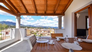 Une table en bois, dressée pour un repas, est placée sur un balcon offrant une vue sur les montagnes.
