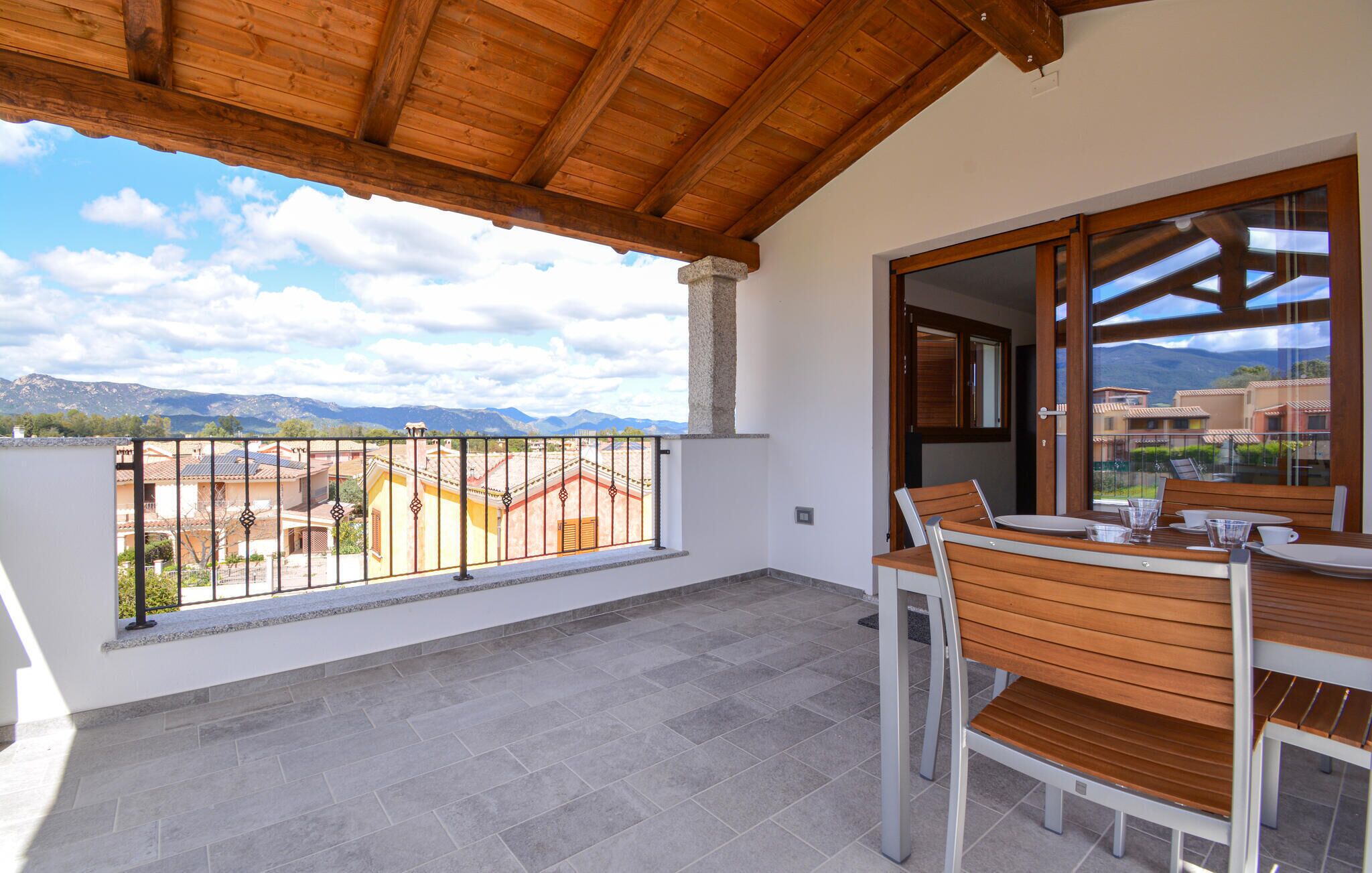 A balcony with a wooden ceiling, a table with chairs, and a view of a mountainous landscape.