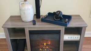 A fireplace with a 'RELAX' sign, a vase with dried plants, a remote control, and a black speaker on a wooden table. - Close to everything-Centrally located to downtown, coliseum, hospital, & stadium (Fayetteville)