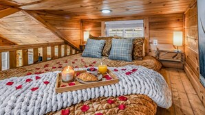 A cozy wooden cabin bedroom with a bed, pillows, a bedside table with a lamp, and a window. - The Lookout — Romantic Tiny Home w/ Mountain Views (Sevierville)