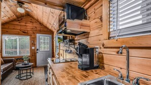 A cozy cabin-style kitchen with wooden walls, a built-in stove, and a large window. - The Lookout — Romantic Tiny Home w/ Mountain Views (Sevierville)