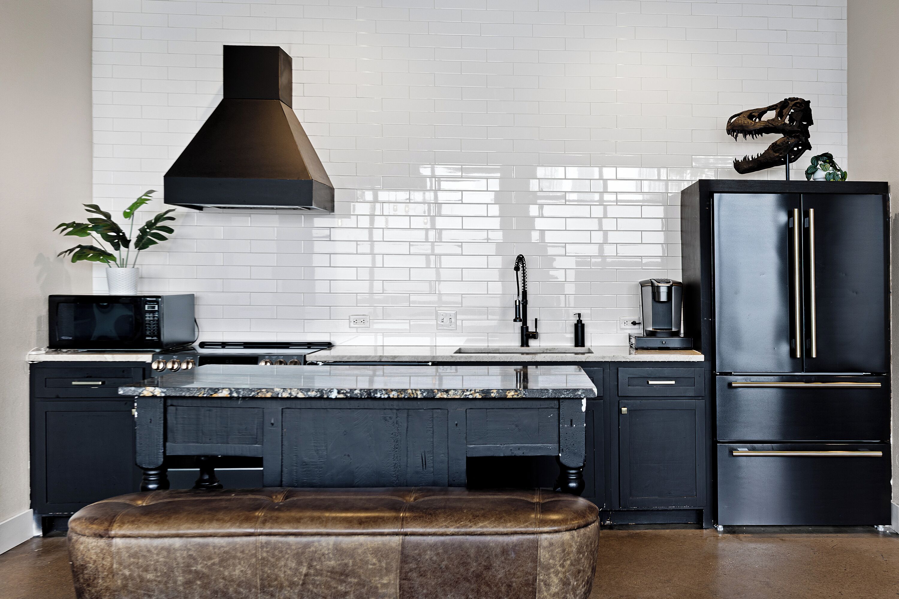 A modern kitchen with a black stove, microwave, and refrigerator, a white tiled backsplash, and a plant on the counter.