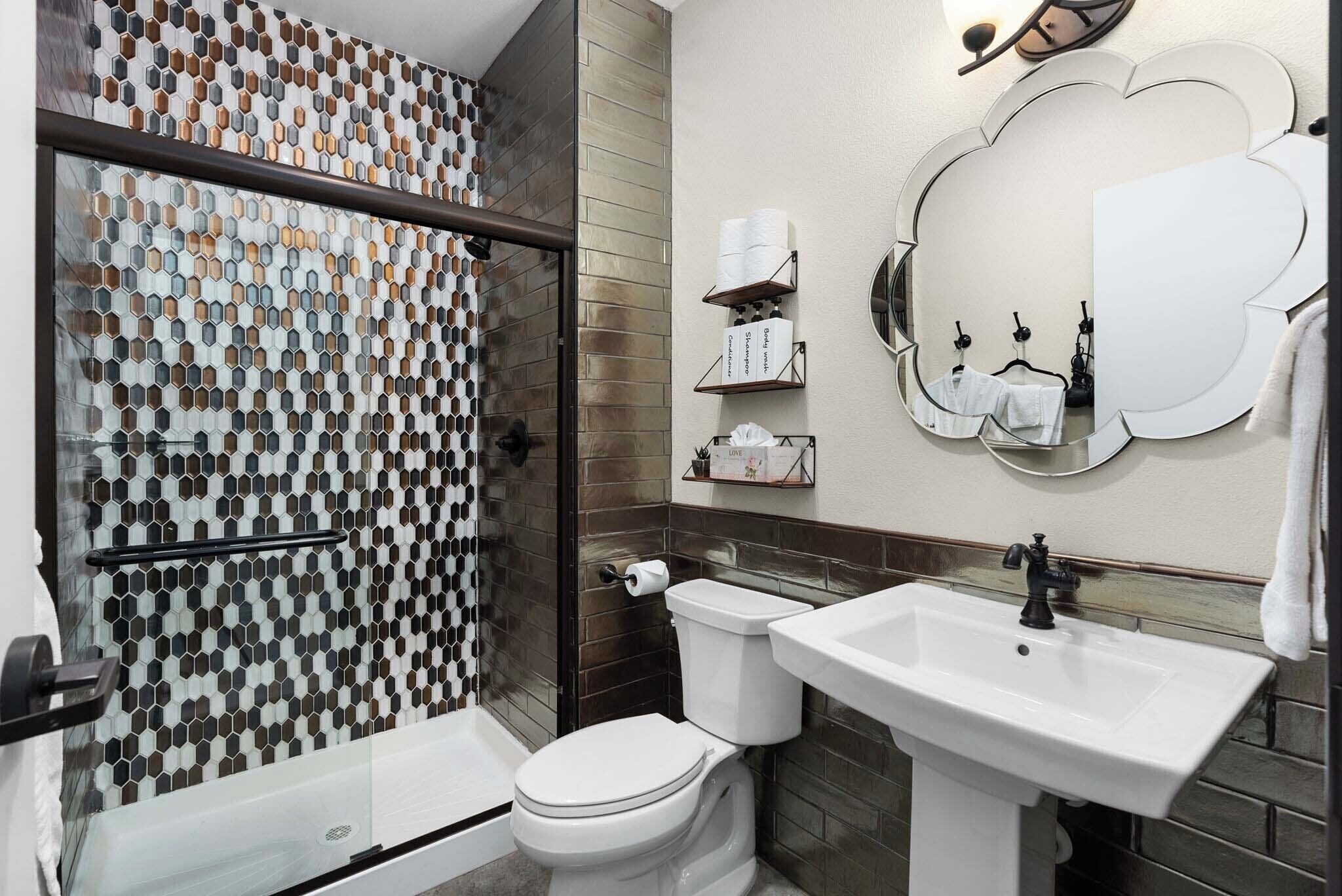 Ein Badezimmer mit Dusche, Toilette, Waschbecken und einem Spiegel mit Wolkenform.