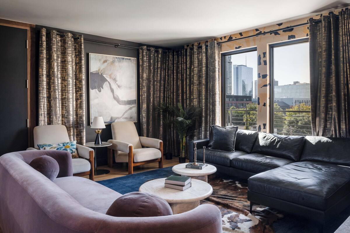 A modern living room with a sofa, armchair, and coffee table, featuring a city view through large windows.