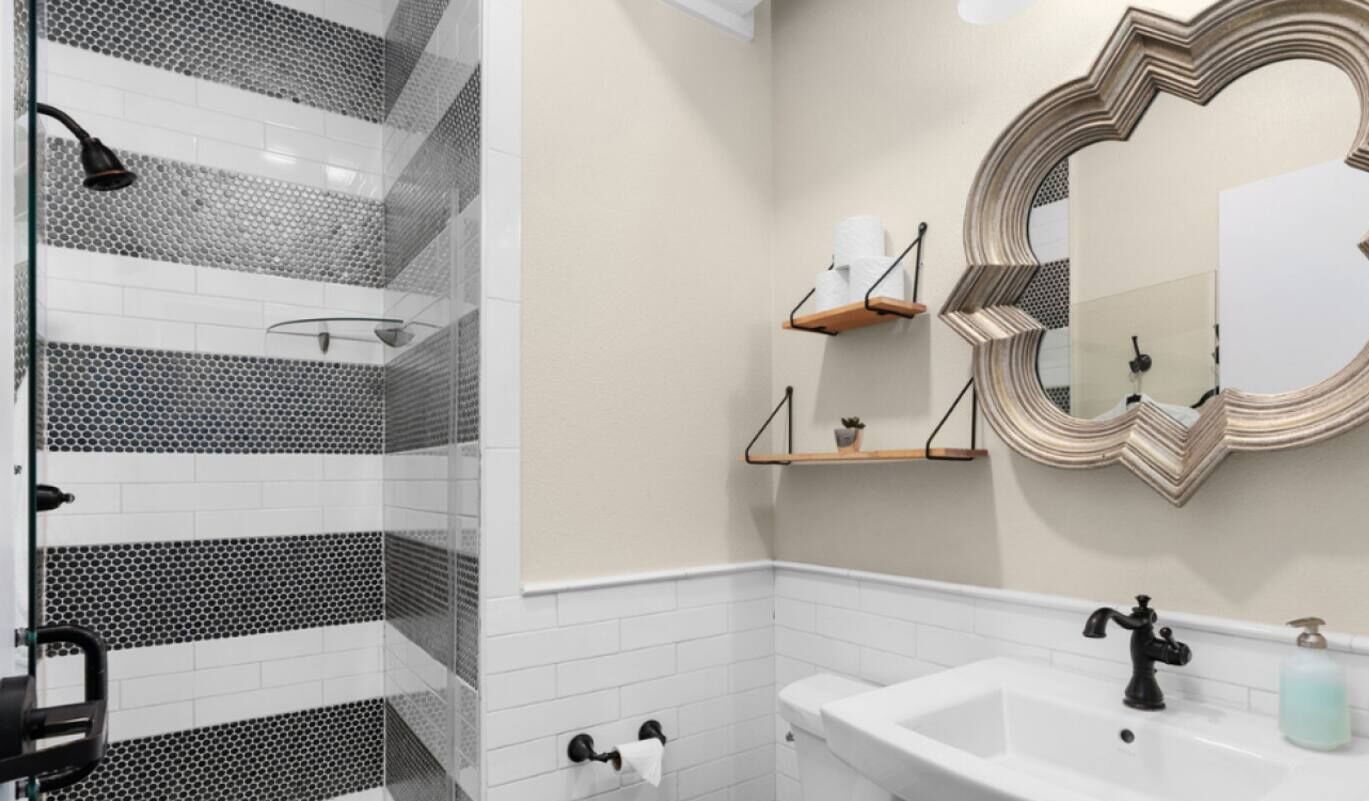 A bathroom with a shower, toilet, sink, and a decorative mirror.
