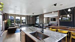 A modern kitchen with a marble countertop, a sink, and a dining area with yellow chairs. - Inn Cahoots (Austin)
