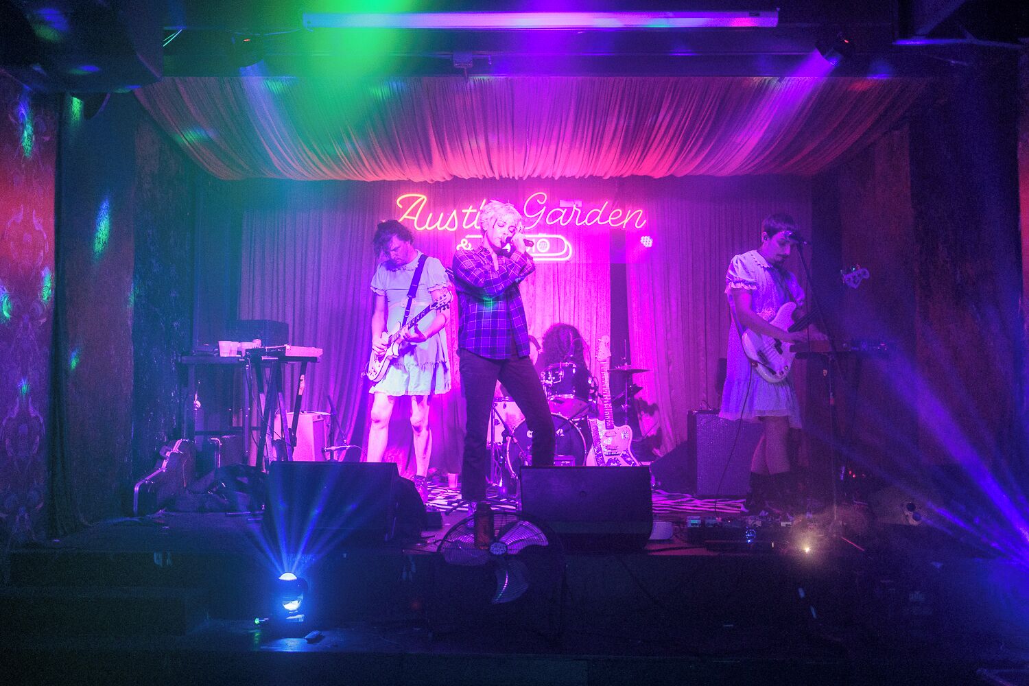 A band performing on a stage with a neon sign reading "Austin Garden".