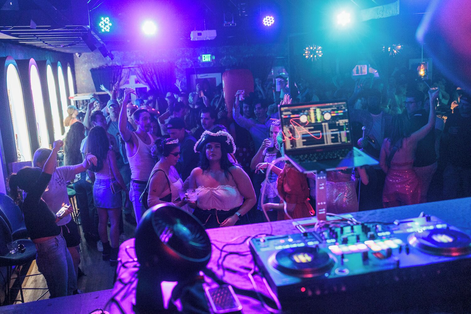 A crowded indoor event with a DJ booth and people dancing.