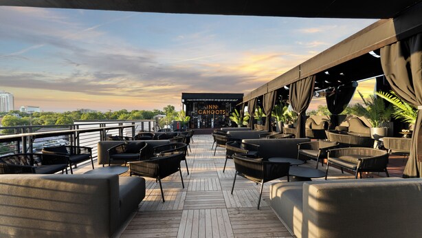 A deck with outdoor seating, a sign for 'Inn Cahoots', and a view of the city skyline. - Inn Cahoots (Austin)