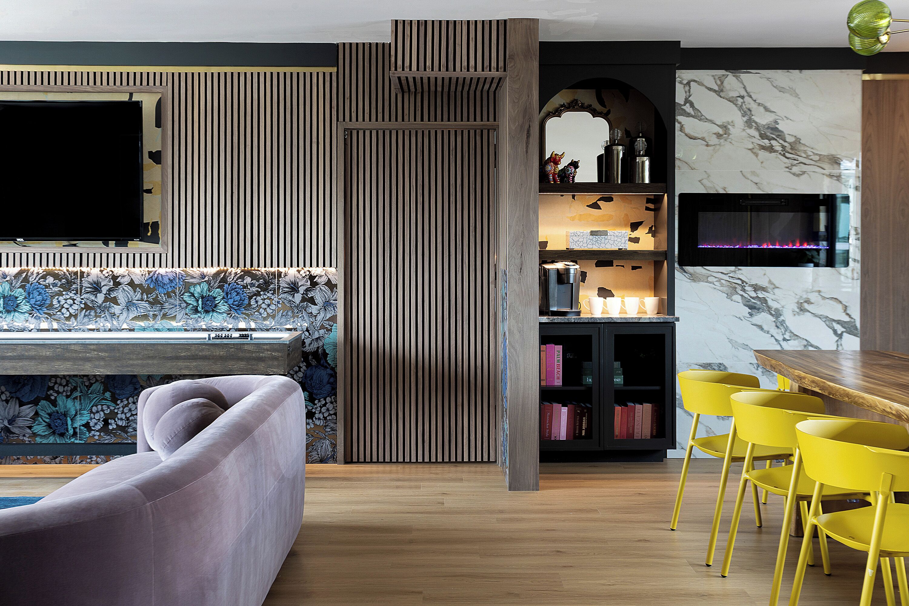 Ein modernes Wohnzimmer mit einer Couch, einem Holzespeisetisch mit gelben Stühlen, einem Kamin und einem an der Wand befestigten Fernseher.