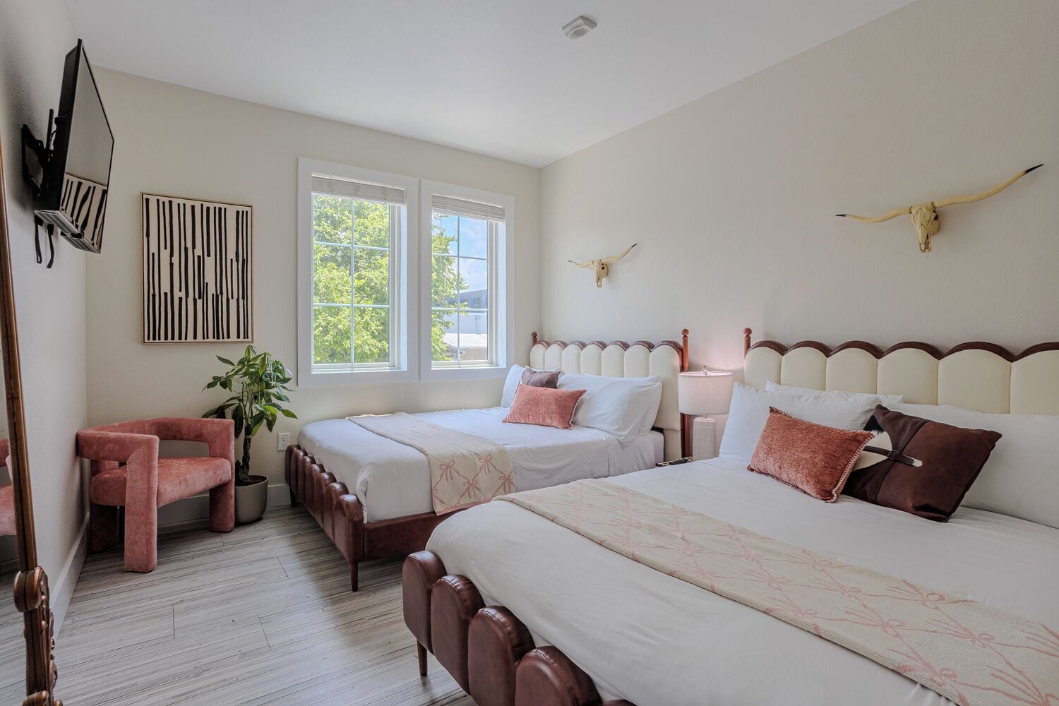 A hotel room with two beds, a TV, a plant, and a bull skull decoration.