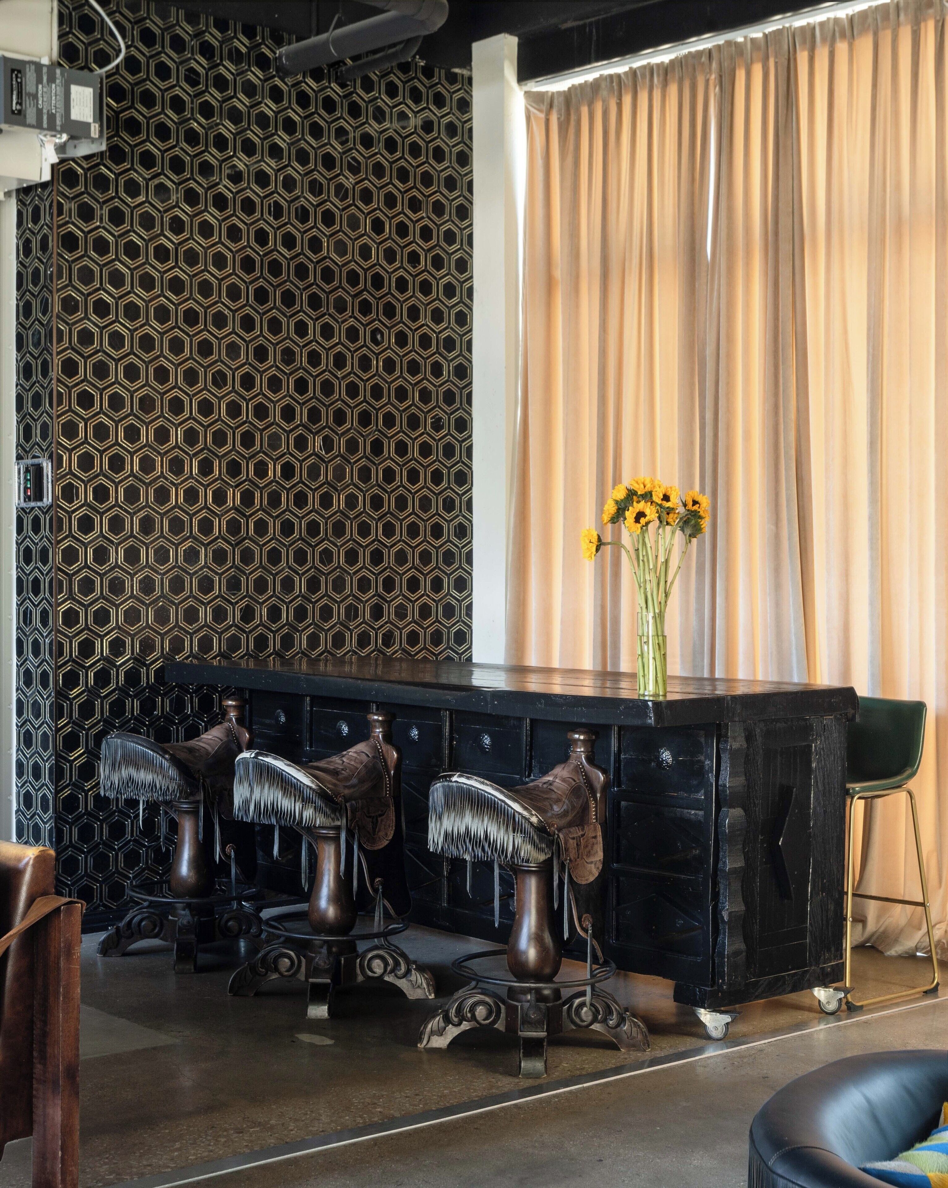 A room with a patterned wall, a black console table with a vase of sunflowers, and a green chair.