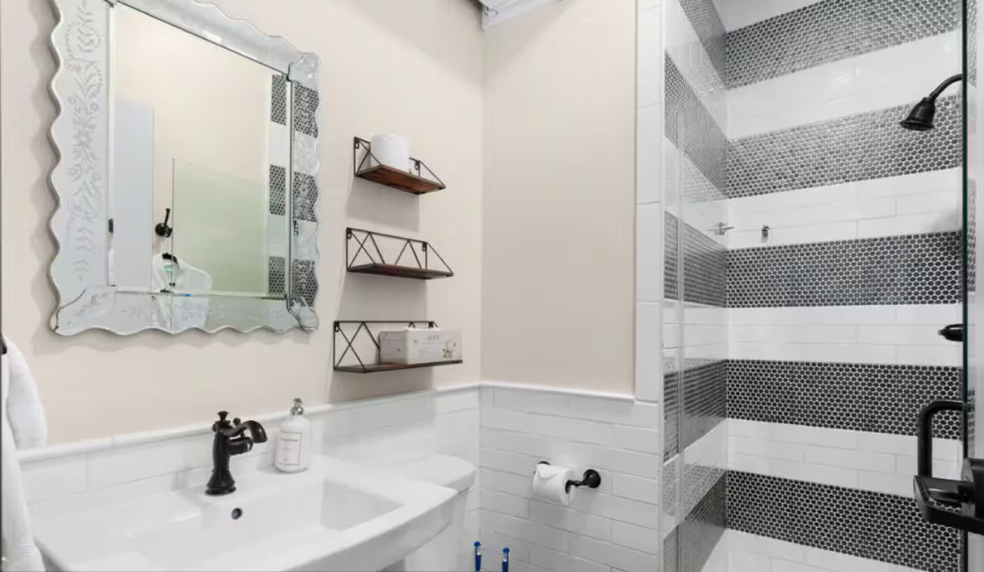 Ein komplettes Badezimmer mit Waschbecken, Spiegel und Toilette, sowie einer Dusche mit schwarz-weißen Fliesen.
