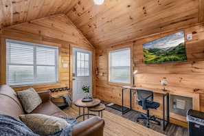 L’intérieur chaleureux d’un chalet, avec un décor en bois, un canapé, une petite table, un bureau et un tableau accroché au mur.