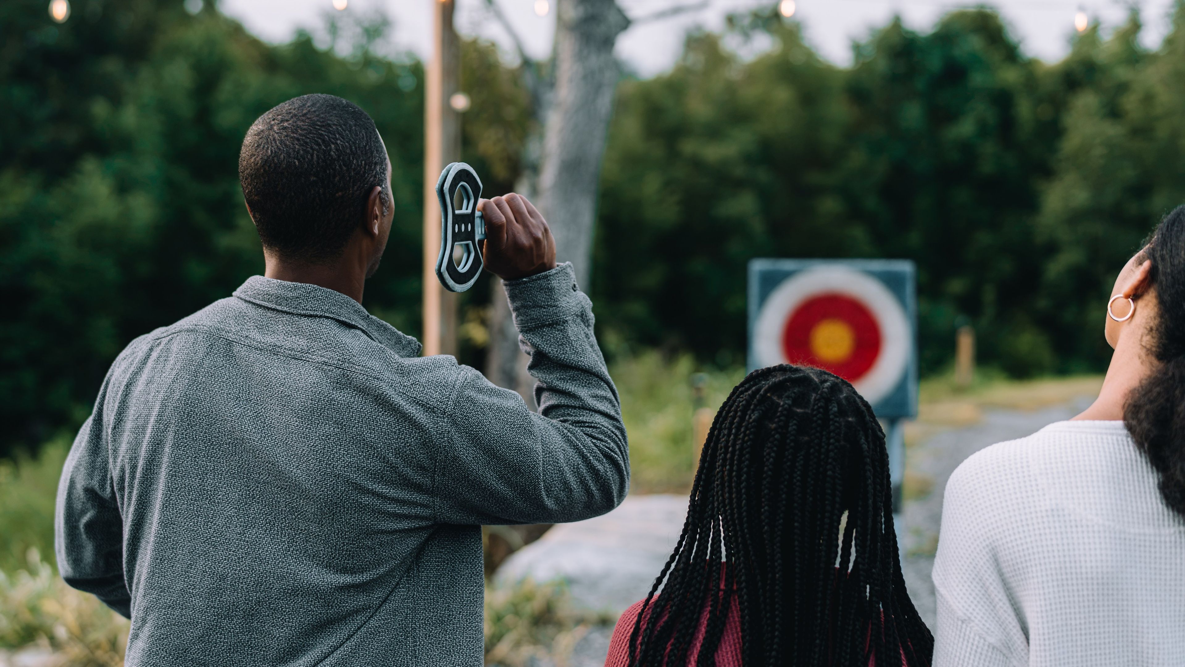 A person holding a circular object, possibly a camera or a lens, with a target sign in the background.